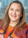 Headshot of heather barger who has long blonde hair, wearing an 
organge and black blouse and there is a blurred background